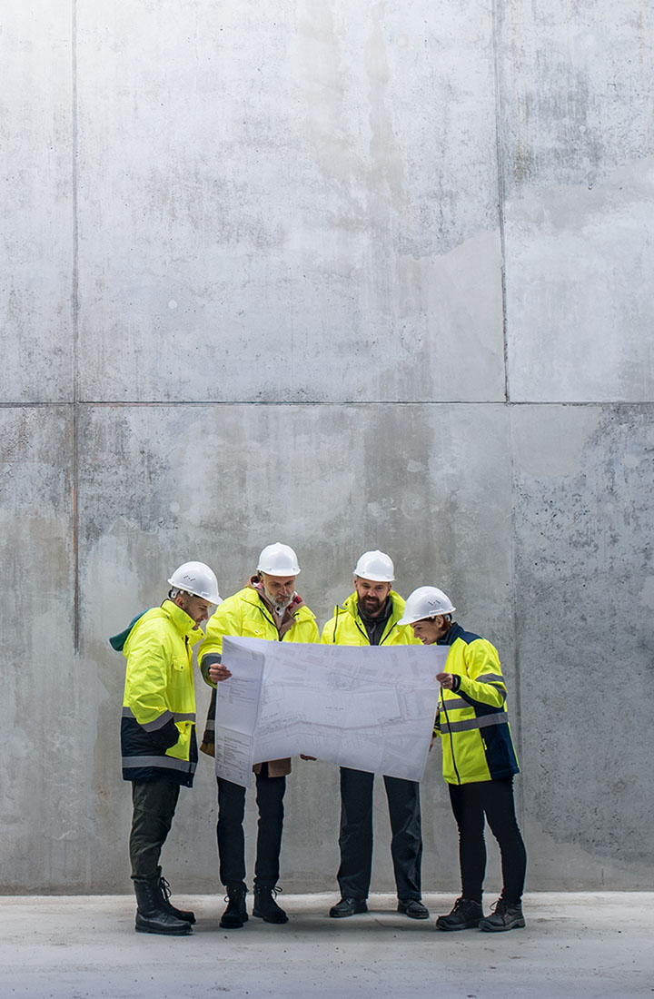 Group of construction contractors glances together at a plan in front of a large concrete building
