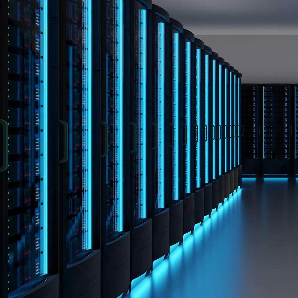 A long shot down a data center aisle with rows of black server racks with blue lights shining.