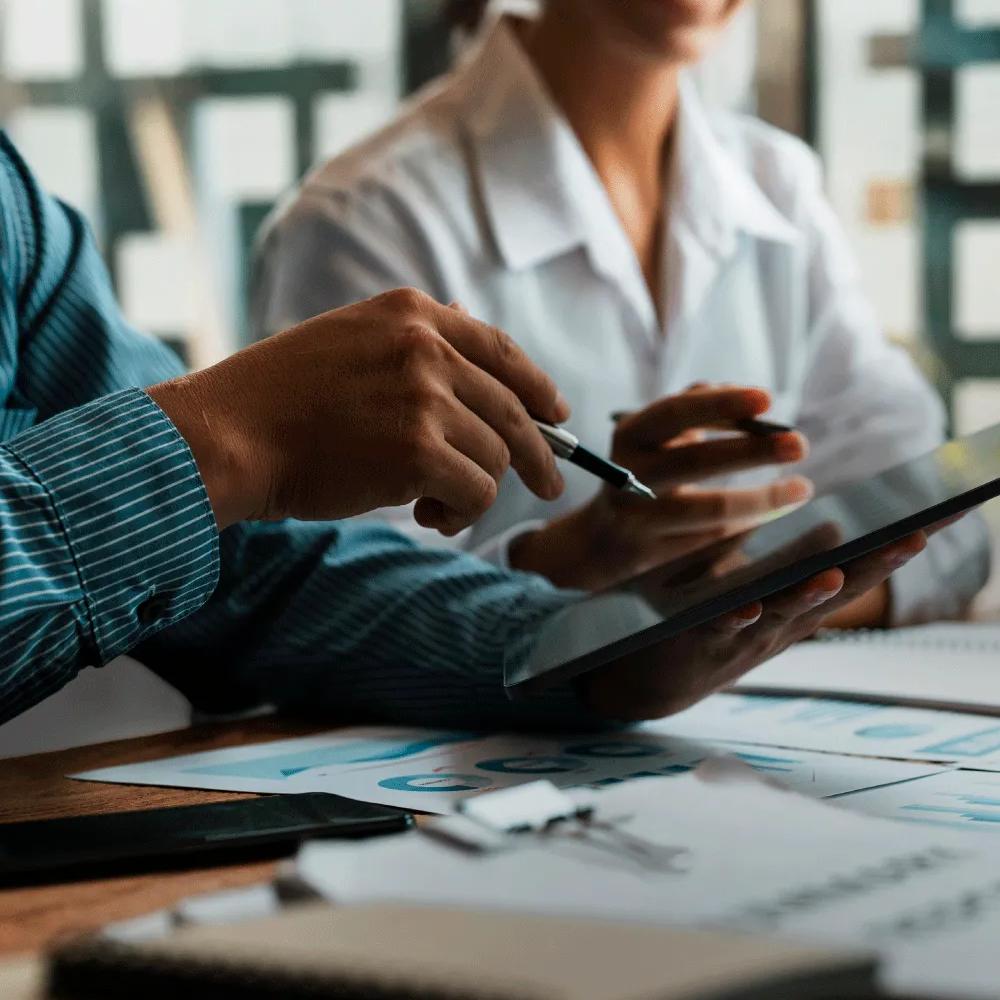 A person holding a tablet with another person in a desk with papers and notebooks