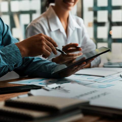 Deux travailleurs regardant une tablette. On voit des ordinateurs portables et des ordinateurs affichant des graphiques sur la table sur laquelle ils travaillent.