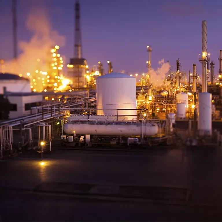 Panoramic view of a lit up refinery at night with a purple sky.
