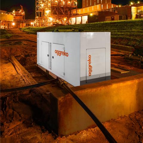 A night scene featuring an industrial container unit with "Aggreko" branding, surrounded by illuminated infrastructure and wet ground.