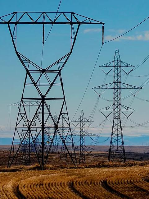 Vue aérienne de plusieurs pylônes de transmission dans un champ herbeux, sous un ciel bleu.