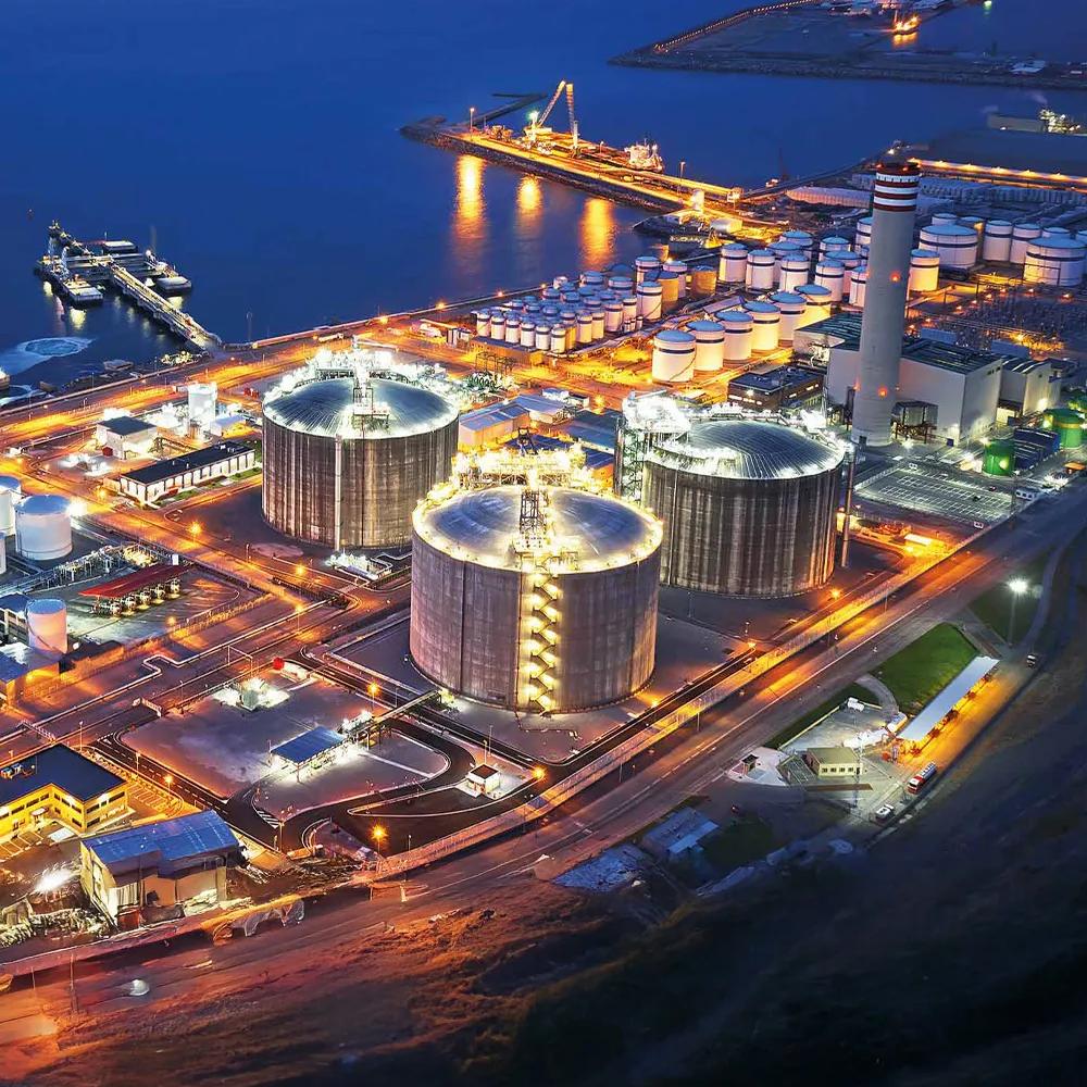 An aerial panoramic night view of a refinery situated on a dark waterfront.