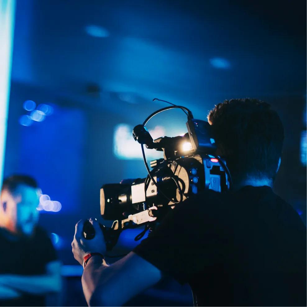 A person holding a professional video camera, recording a person in a set.