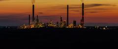 distant view of silhouette of oil refinery lit with sparkling Christmas-like lights, smoking towers and buildings against colourful night sky, looking like a distant illuminated city