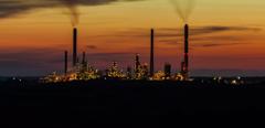 distant view of silhouette of oil refinery lit with sparkling Christmas-like lights, smoking towers and buildings against colourful night sky, looking like a distant illuminated city