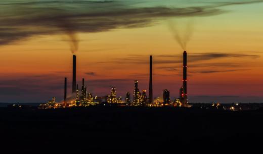 distant view of silhouette of oil refinery lit with sparkling Christmas-like lights, smoking towers and buildings against colourful night sky, looking like a distant illuminated city