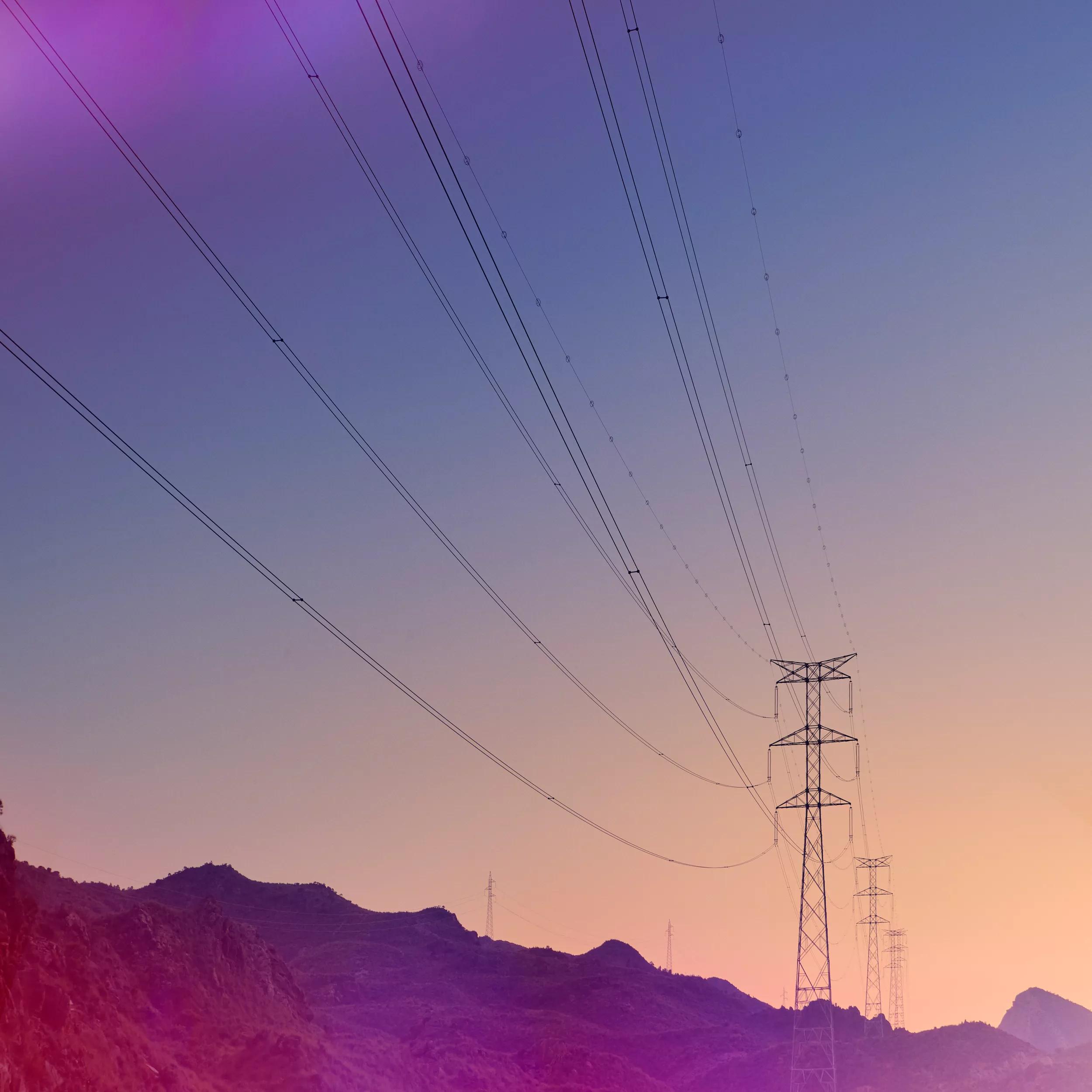 Power lines stretch across a gradient sky at sunset over silhouetted mountains.
