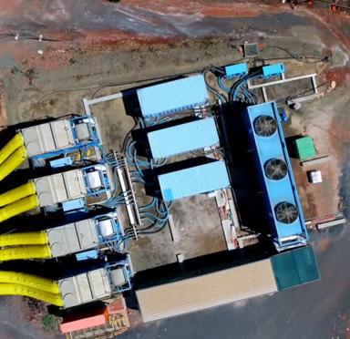 Aerial view of an industrial site featuring multiple large aggreko cooling units, yellow pipes, and cooling units on a dirt surface.