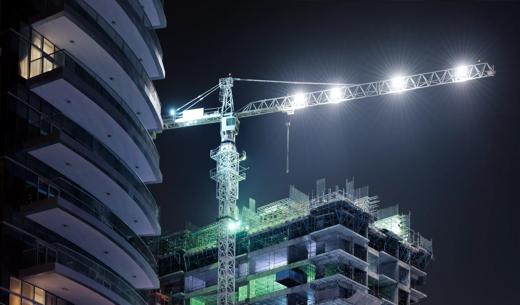 illuminated tower crane at skyscraper construction site at night