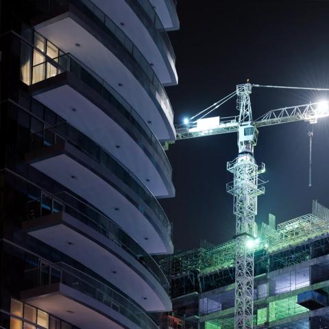 illuminated tower crane at skyscraper construction site at night