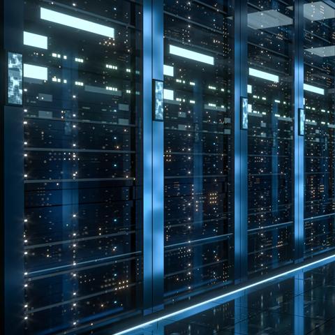 A close-up view of a row of tall, dark server racks in a data center. Small, glowing, rectangular screens are mounted vertically on the rack exteriors, displaying bright light blue data streams.