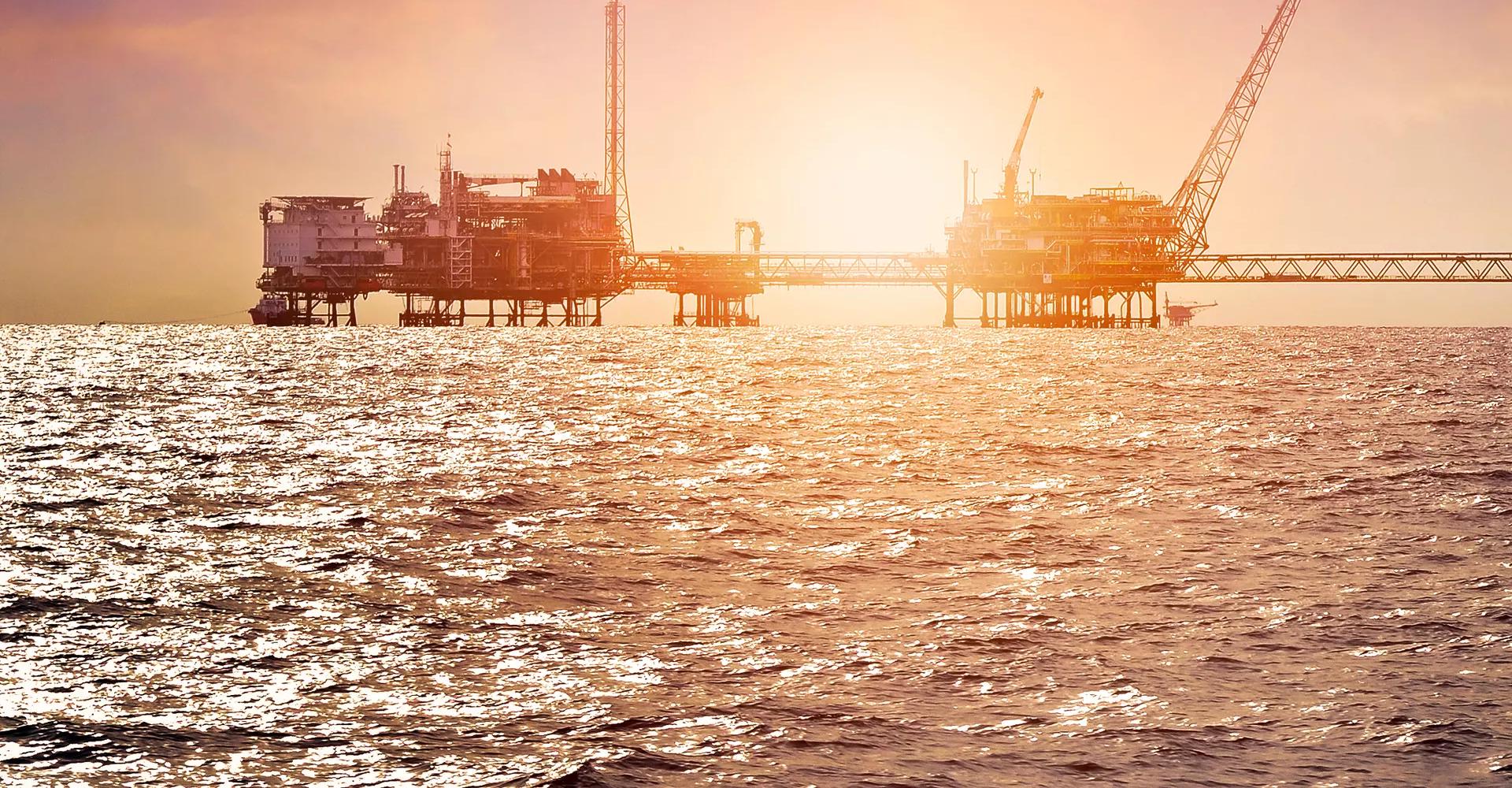 Offshore oil drilling platform with cranes, equipment, and support vessels in blue water.