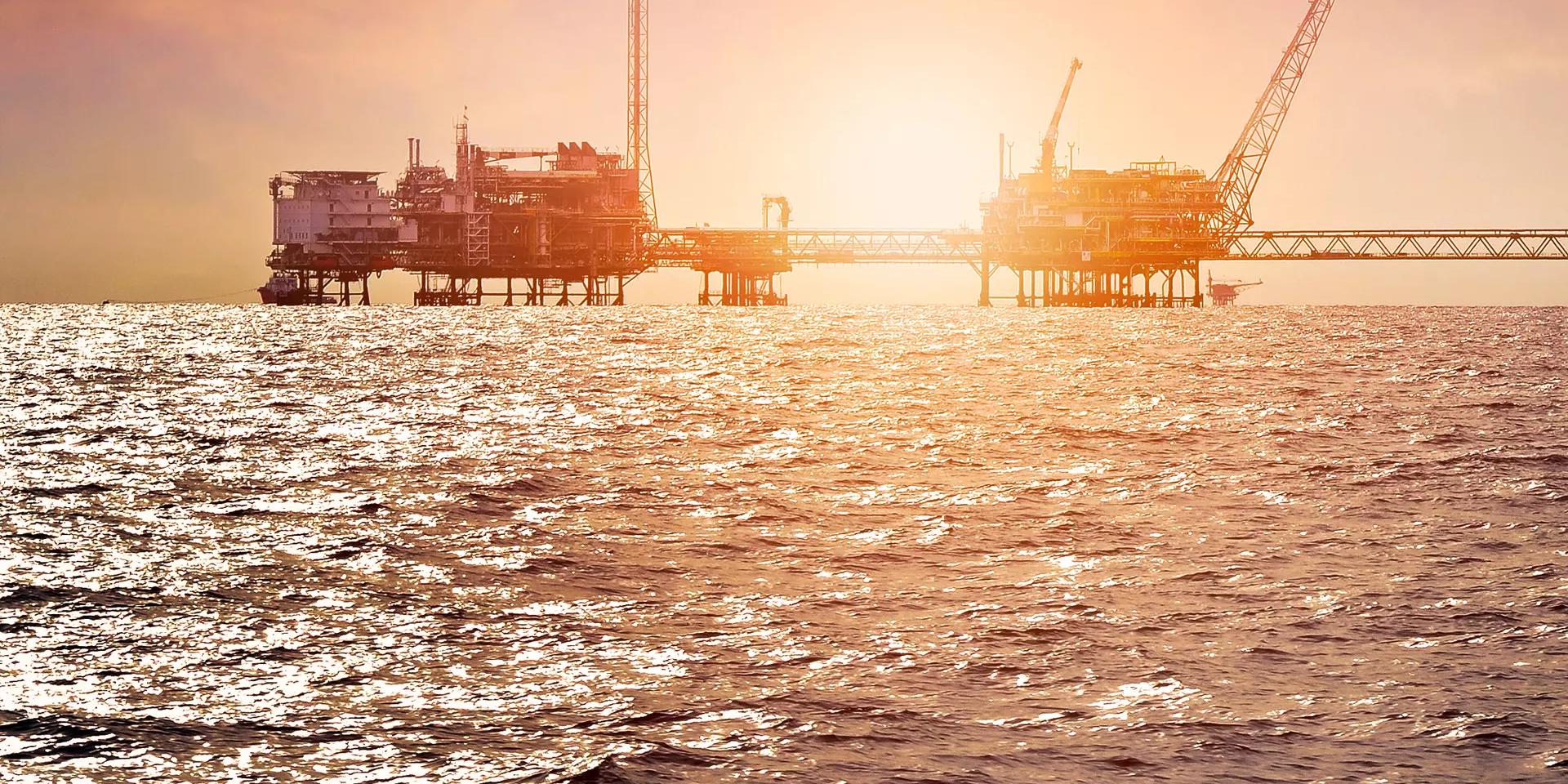 Offshore oil drilling platform with cranes, equipment, and support vessels in blue water.