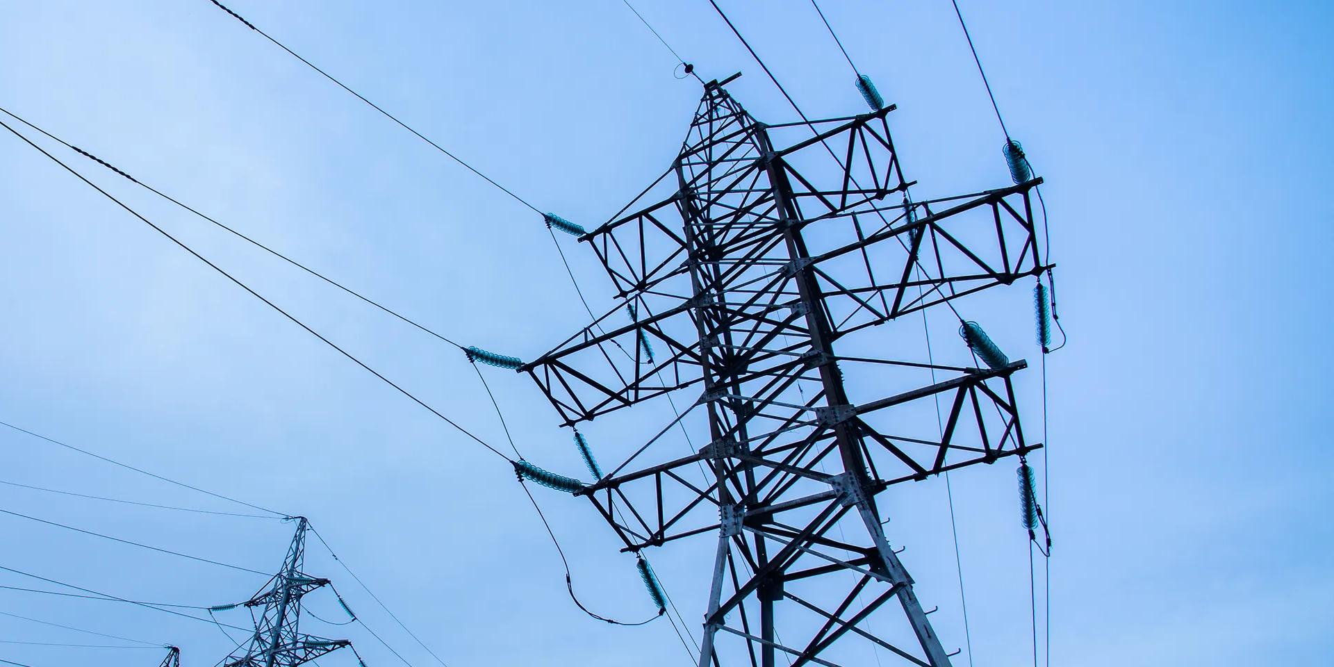 Three transmission towers against a blue sky, and rows of more towers in the background 