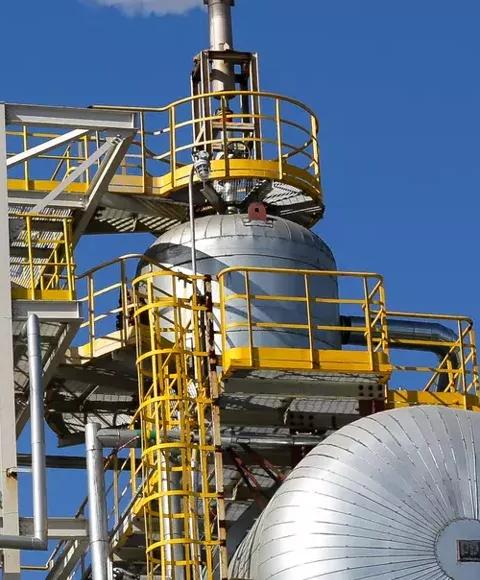 View of the top of a refinery tower against a blue sky.
