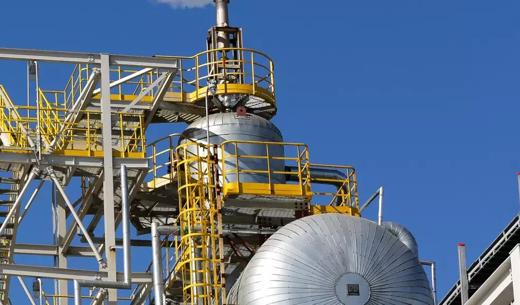 Metal pipes and an industrial framework with a yellow staircase against a clear blue sky.
