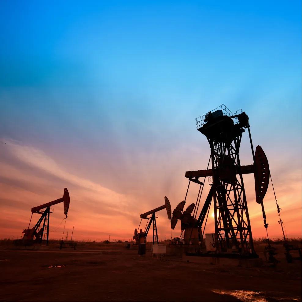 A yellow and blue oil pump jack stands against a backdrop of clouds and a blue sky in an open landscape.