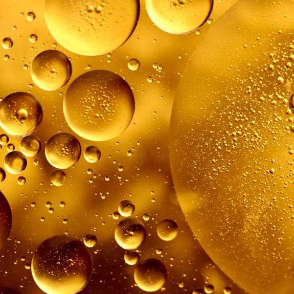 Full frame macro photography of gold-colored water and oil, forming an abstract pattern of circles and bubbles.