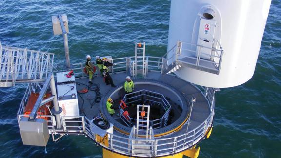 Five workers with safety gear on pulling cables on a ship in the middle of the sea