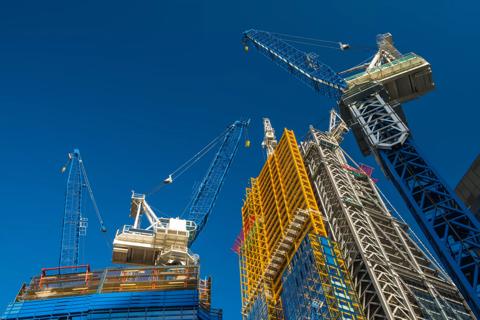 Construction site with multiple cranes and a partially completed high-rise building against a clear blue sky.