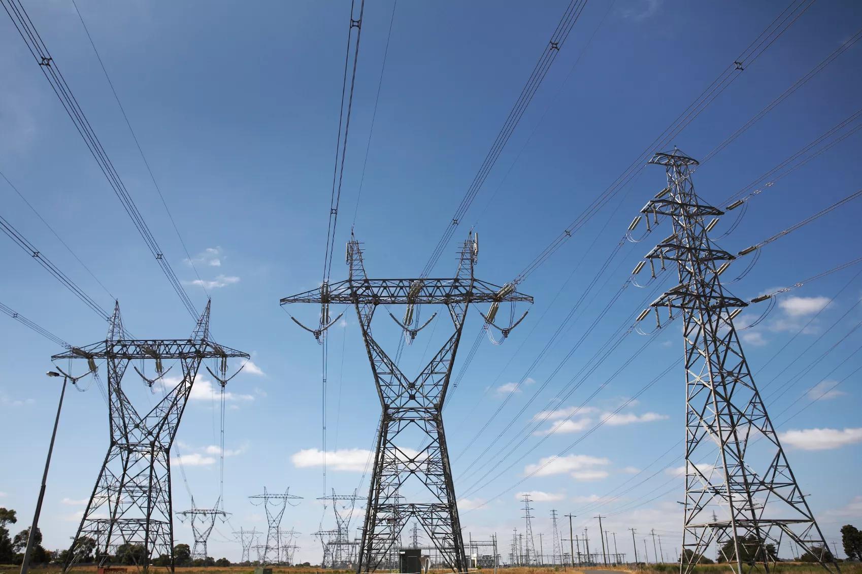 Three transmission towers against a blue sky, and rows of more towers in the background