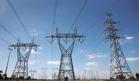 Three transmission towers against a blue sky, and rows of more towers in the background 