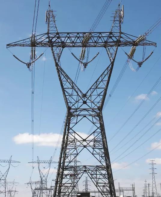 Three transmission towers against a blue sky, and rows of more towers in the background 