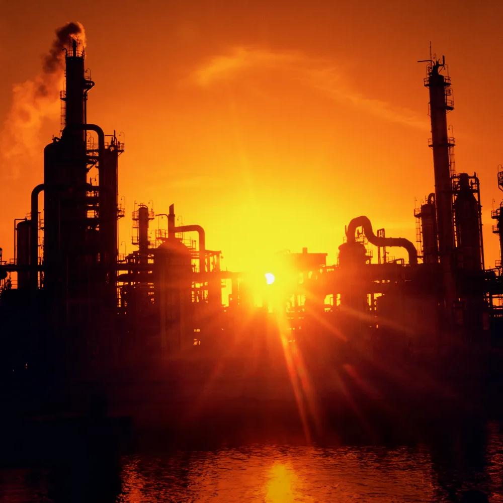 View of a refinery's silhouette against an orange sunset.