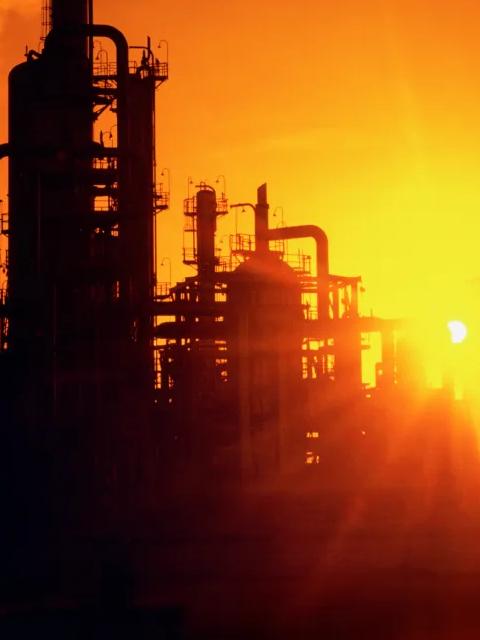 Vue de la silhouette d’une raffinerie sur un coucher de soleil orange.