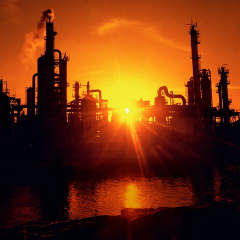 View of a refinery's silhouette against an orange sunset.