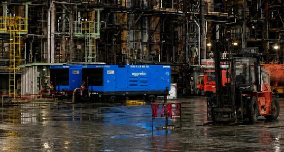 Two blue Aggreko power generators and other industrial equipment inside a manufacturing facility.