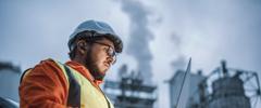 A shot of an young engineer wearing a helmet and using a laptop and hands free device during his night shirt in the oil rafinery. Engineering concept.