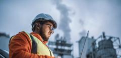 A shot of an young engineer wearing a helmet and using a laptop and hands free device during his night shirt in the oil rafinery. Engineering concept.