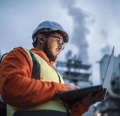 A shot of an young engineer wearing a helmet and using a laptop and hands free device during his night shirt in the oil rafinery. Engineering concept.