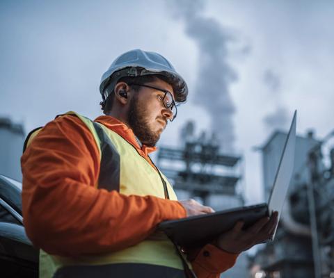 A shot of an young engineer wearing a helmet and using a laptop and hands free device during his night shirt in the oil rafinery. Engineering concept.