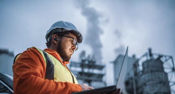 A shot of an young engineer wearing a helmet and using a laptop and hands free device during his night shirt in the oil rafinery. Engineering concept.