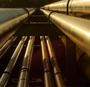 A close-up of a metal pipe with red valves, surrounded by yellow pipes against a clear blue sky.