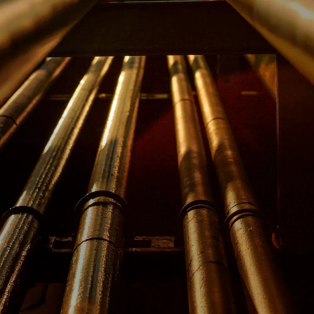 A close-up of a metal pipe with red valves, surrounded by yellow pipes against a clear blue sky.