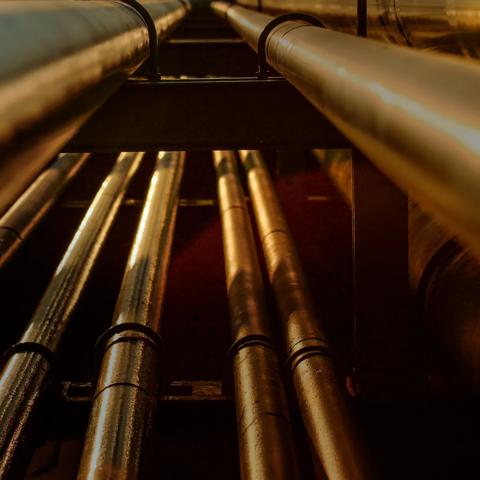 A close-up of a metal pipe with red valves, surrounded by yellow pipes against a clear blue sky.
