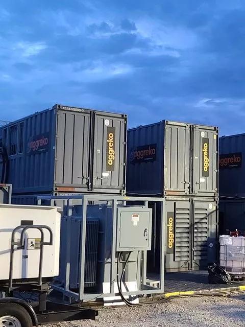 A row of tall, modular gray industrial container units stacked against a moody blue sky.