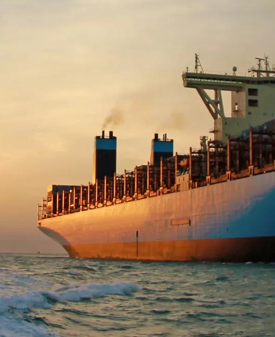 A large cargo ship is on the water during sunset.
