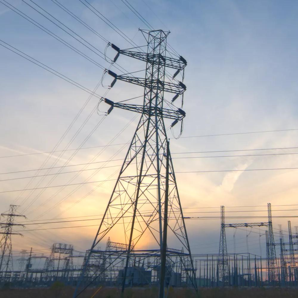 Power lines and tall transmission towers silhouetted against a colorful sunset sky.