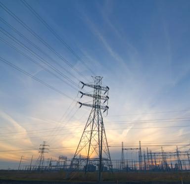 Power lines and tall transmission towers silhouetted against a colorful sunset sky.
