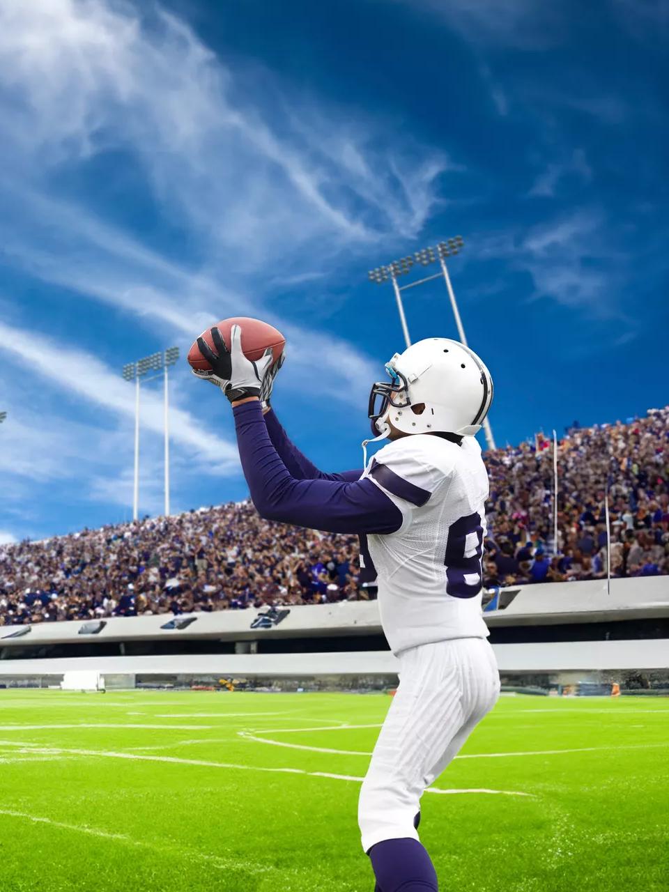A professional football player in a stadium catching the ball in front of full bleachers under a blue sky.