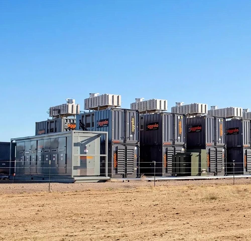 Several rows of stacked, black industrial units in a dessert.