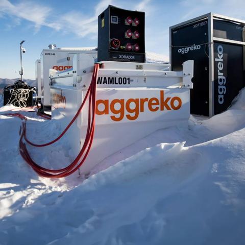 Panoramic view of a white Aggreko fuel tank with the orange logo with more Aggreko equipment at the top of a snowy mountain with trees