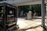 A black transformer with the logo Aggreko is placed near a pathway, surrounded by greenery and utility equipment.