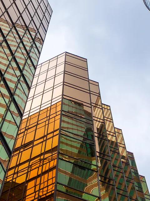 A view from below of modern glass skyscrapers with bright, reflective turquoise panels.